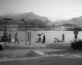 People are standing in front of the fjord in different positions. Waiting, raising their arms, walking, taking pictures, in the background snowy mountains