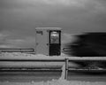 Snow-covered roadside booth with a blurred vehicle passing by on a cloudy day.