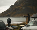 Two people by the Ocean in Unstad with mountains in the background, one person pointing towards the water.
