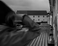 Black and white photo of a boat on a dock captured through arms of a person who walkes by